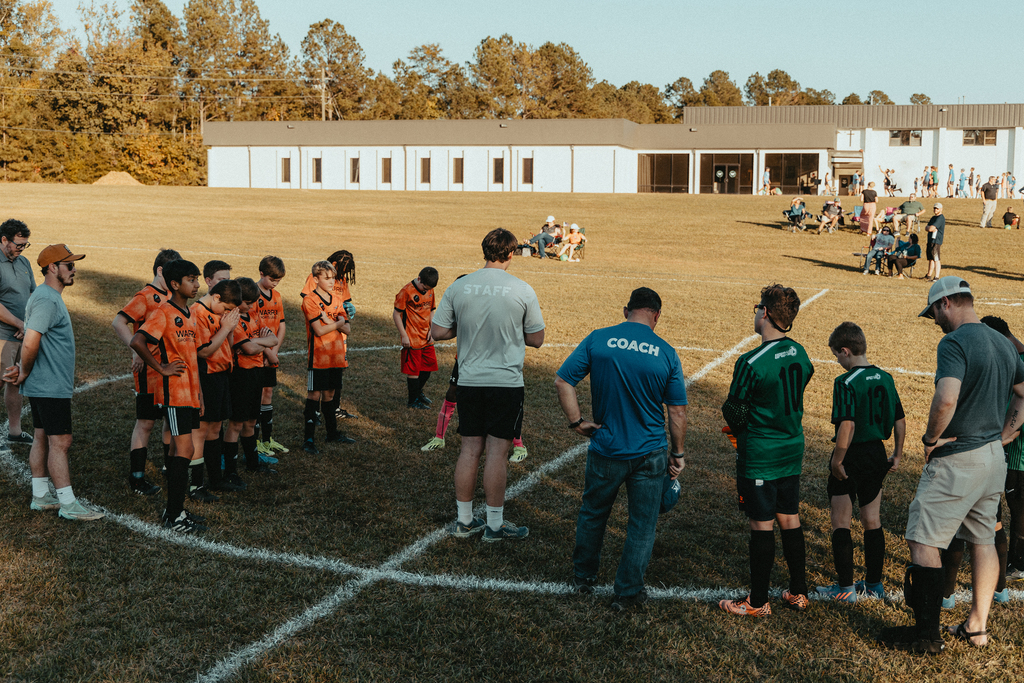 Coaches, staff and young soccer players stand with heads bowed on a field at Warren.
