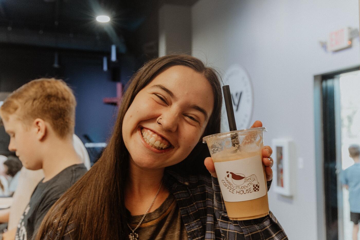 A teenage girl grinning and holding up an iced drink at Midweek at Warren.