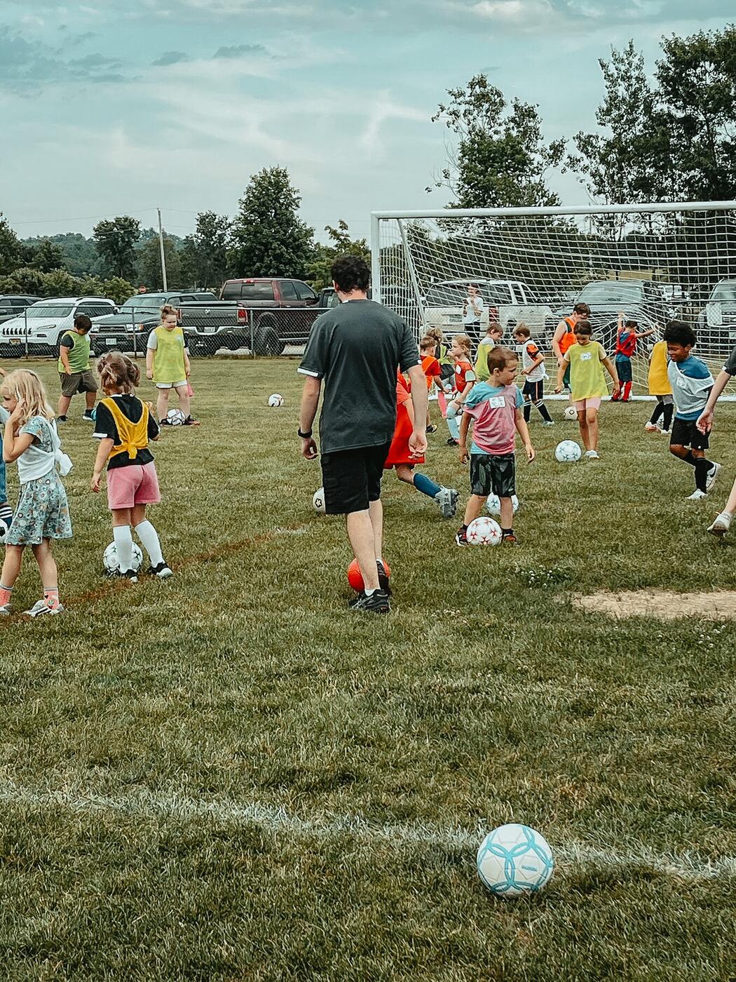 Children with soccer balls on a field, a coach among them.