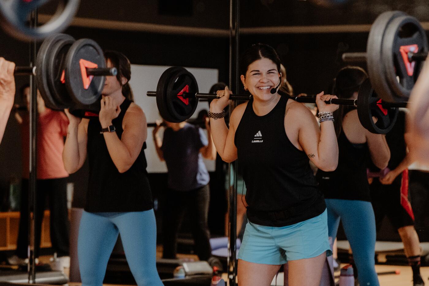 Members pressing barbells overhead in class.